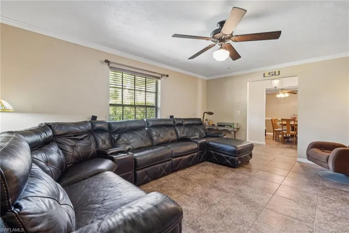 Living room featuring tile floors, ceiling fan, and ornamental molding