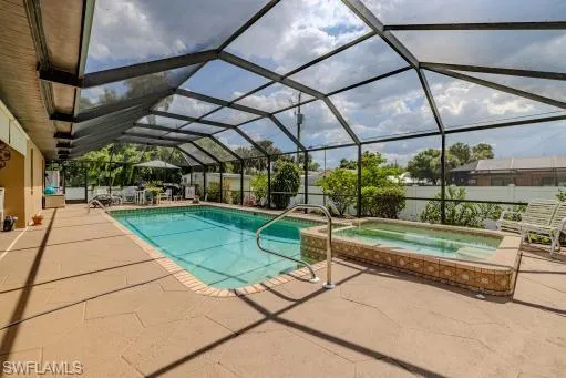 View of swimming pool featuring a patio area, glass enclosure, and an in ground hot tub