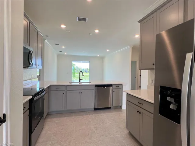 Kitchen with appliances with stainless steel finishes, gray cabinets, a peninsula, light countertops, and light tile patterned floors