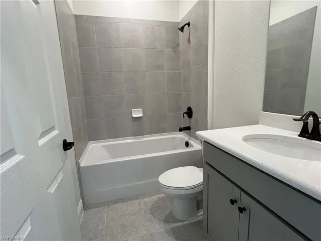 Bathroom featuring vanity, a textured wall, shower / bath combination, and tile patterned floors