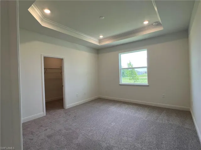 Carpeted empty room featuring crown molding, a raised ceiling, and recessed lighting