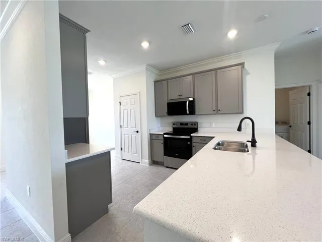 Kitchen featuring appliances with stainless steel finishes, gray cabinets, ornamental molding, light stone counters, and a peninsula