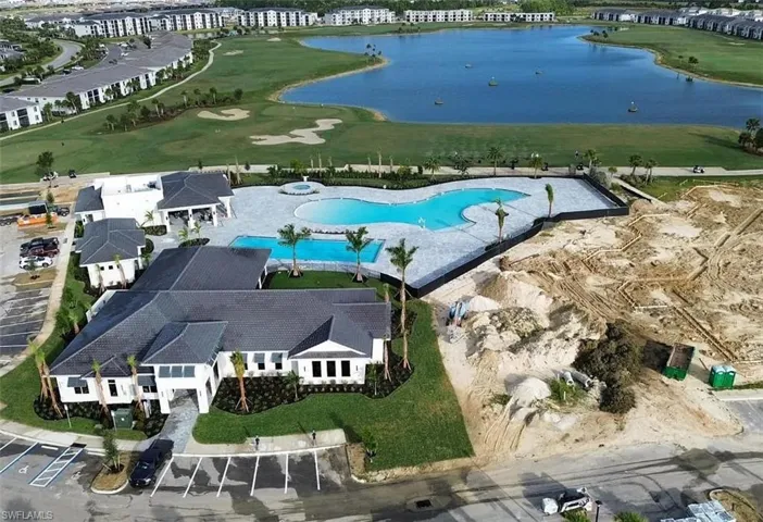 Curved outdoor swimming pool with a large paved deck, surrounded by palm trees and manicured lawns