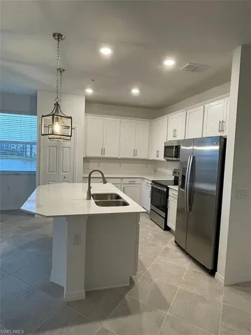 Modern kitchen featuring white cabinetry, stainless steel appliances, a white island with an undermount double sink, and a contemporary pendant light fixture