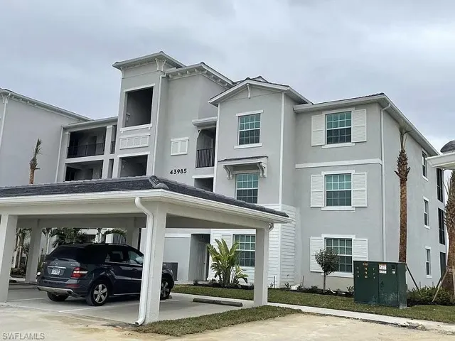 Multi-story residential building featuring light grey stucco exterior and white window shutters