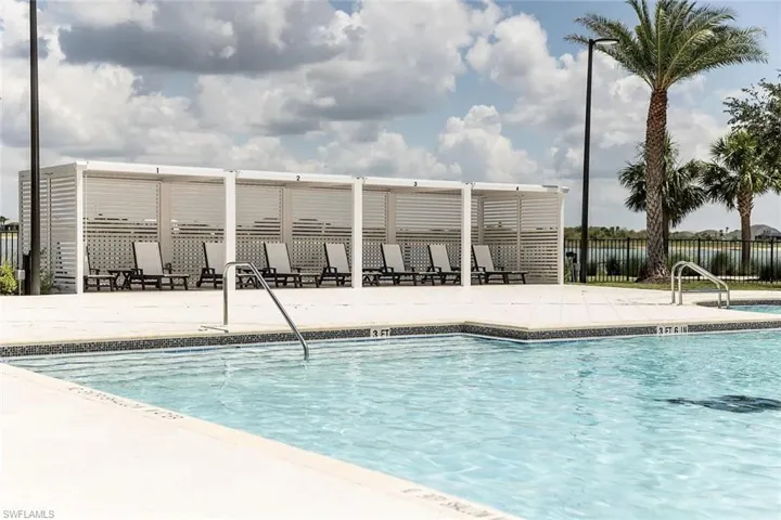 Resort-style pool area featuring a perimeter of white cabanas, a spacious paved deck, and a tropical palm tree