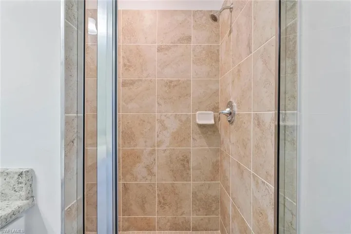 Tiled shower enclosure featuring a chrome shower head and faucet