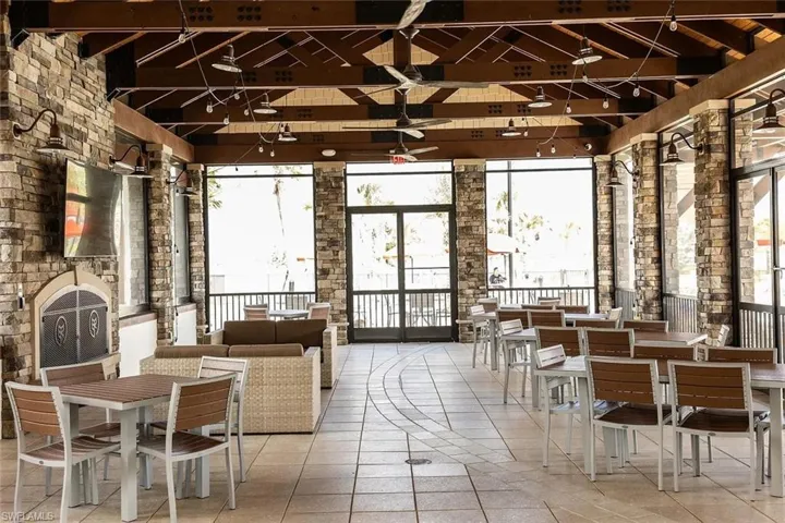 Spacious covered patio featuring a stone-clad fireplace, exposed beam ceiling, tile flooring, and multiple ceiling fans