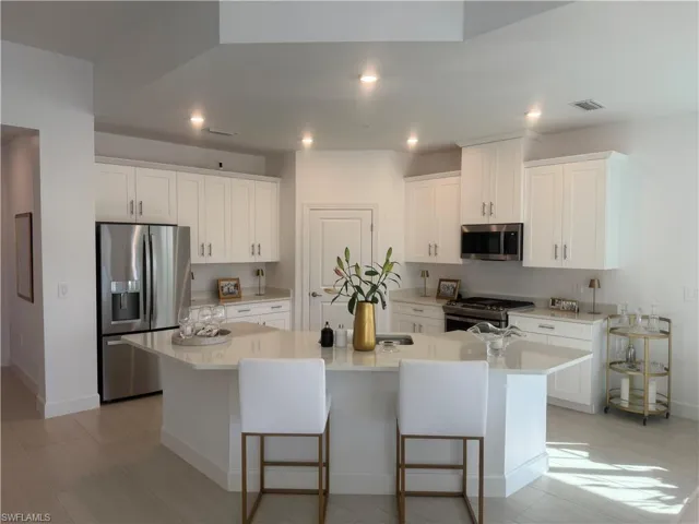 Kitchen with stainless steel appliances, white cabinets, a kitchen bar, an island with sink, and light stone countertops