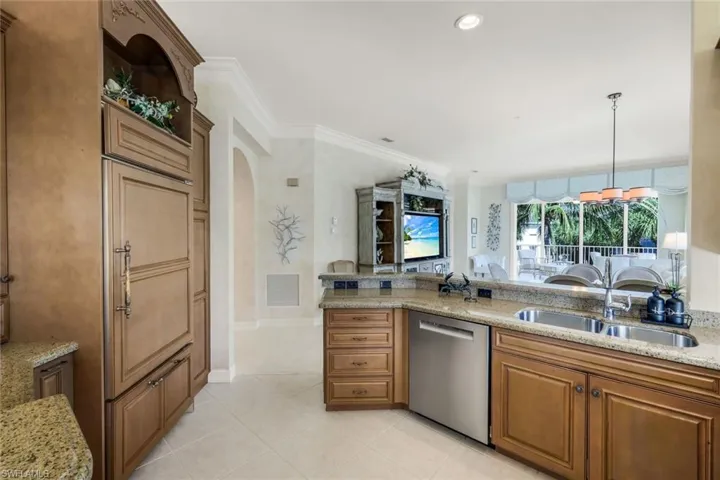 Kitchen featuring light wood cabinetry, stone countertops, stainless steel dishwasher, and built-in panel-front refrigerator