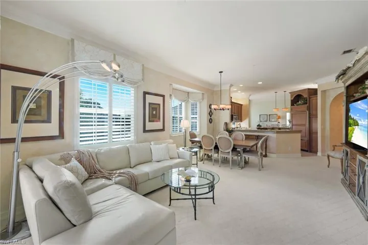 Spacious living area featuring neutral carpeting, crown molding, and plantation shutters