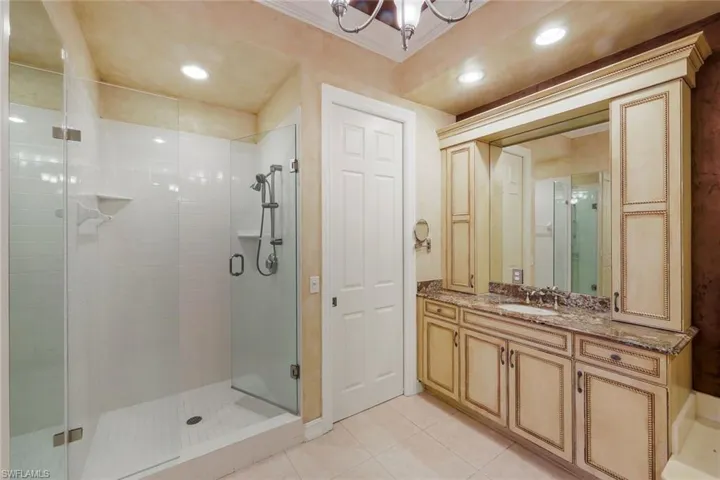 Spacious bathroom featuring a frameless glass shower enclosure with white subway tile, a large vanity with an integrated sink and stone countertop, and ample built-in cabinetry