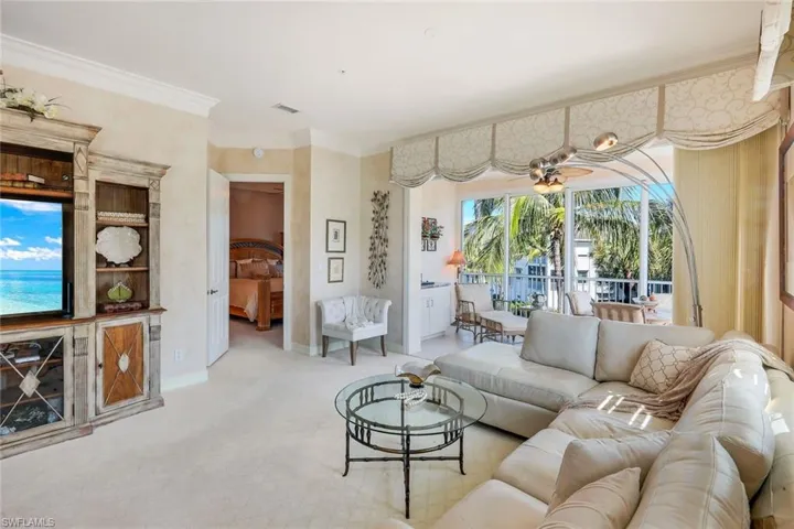 Spacious living area featuring light-toned carpeting, crown molding, and a built-in entertainment center