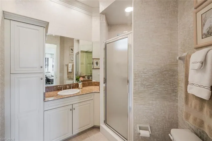 Bathroom featuring a white vanity with an undermount sink and a polished faucet, granite countertop, built-in storage cabinetry, a glass-enclosed shower, and textured wall coverings