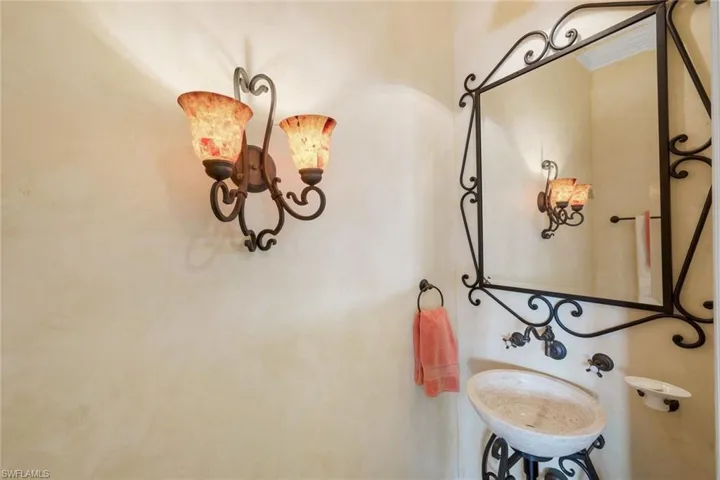 Wrought iron wall sconce with mosaic glass shades, complement by a matching framed mirror and pedestal sink