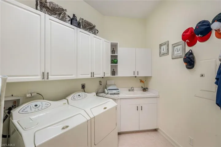 Dedicated laundry room featuring a utility sink, extensive white cabinetry, and light-toned tile flooring