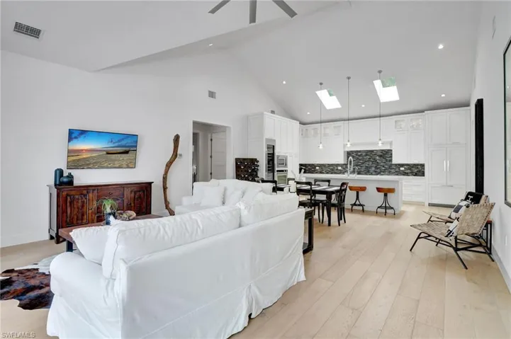 Living area with a skylight, high vaulted ceiling, light wood-style floors, ceiling fan, and recessed lighting