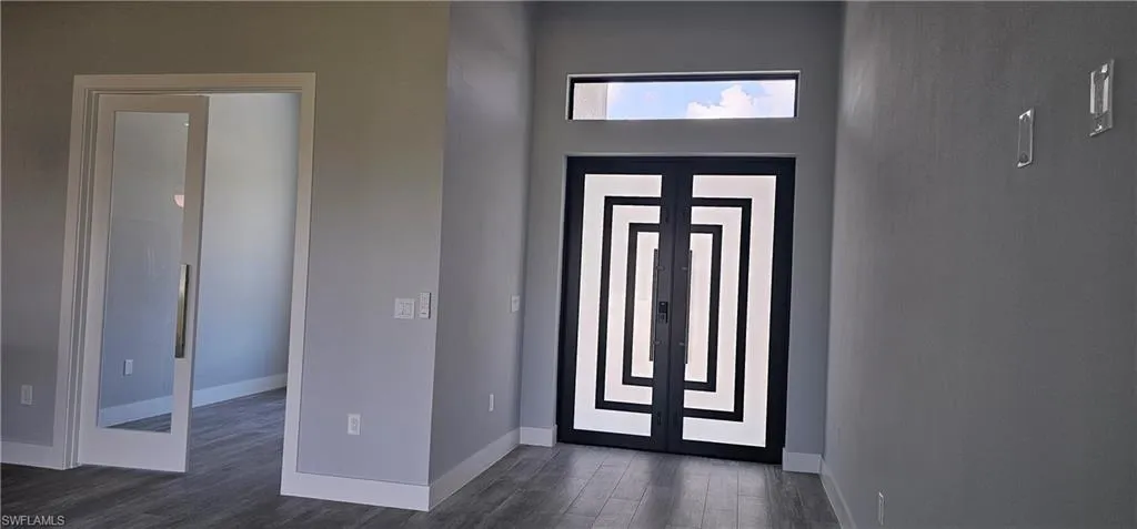Modern entryway featuring a striking geometric-patterned double-door entrance with transom window, polished concrete flooring, and clean white wall finishes throughout the foyer space