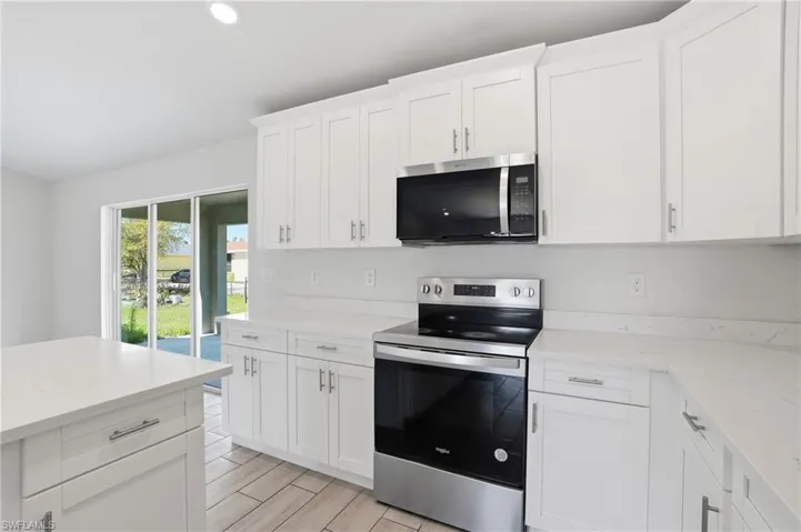 Kitchen with stainless steel appliances, white cabinetry, light stone counters, wood finish floors, and recessed lighting