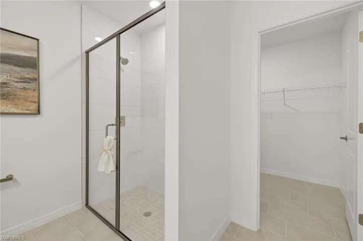 Bathroom with light tile patterned floors, a stall shower, and a walk in closet