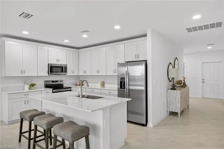 Kitchen with appliances with stainless steel finishes, white cabinets, a breakfast bar area, an island with sink, and recessed lighting