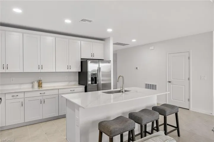 Kitchen with stainless steel fridge, recessed lighting, a breakfast bar, white cabinets, and an island with sink