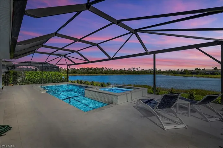Pool at dusk with a patio, an in ground hot tub, a water view, and glass enclosure