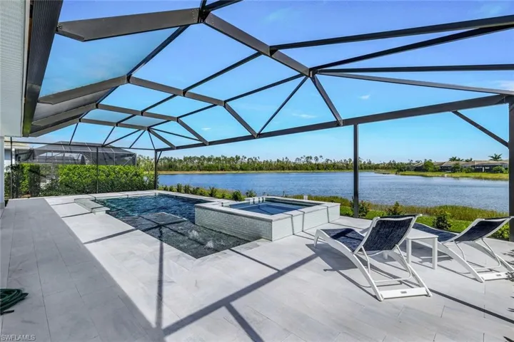 View of pool featuring glass enclosure, a water view, a patio, and an in ground hot tub