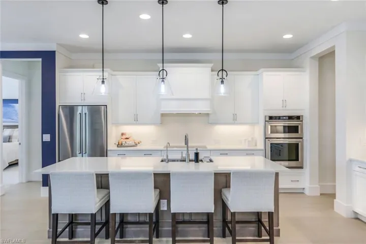 Kitchen with a center island with sink, white cabinets, stainless steel appliances, and decorative light fixtures