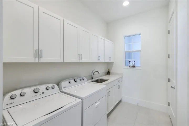 Clothes washing area with light tile patterned flooring, sink, independent washer and dryer, and cabinets