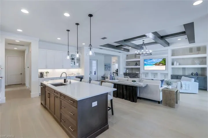 Kitchen featuring beamed ceiling, a kitchen island with sink, sink, white cabinetry, and light hardwood / wood-style flooring