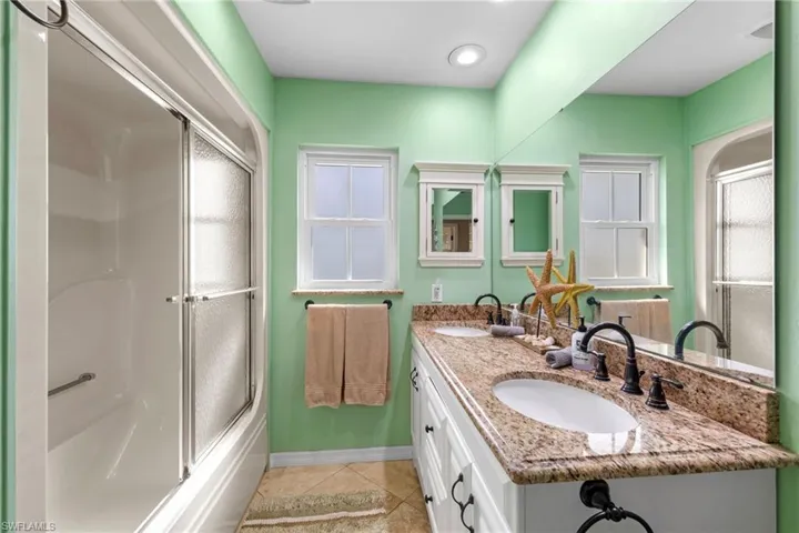 Bathroom featuring light tile patterned floors, double vanity, and enclosed tub / shower combo