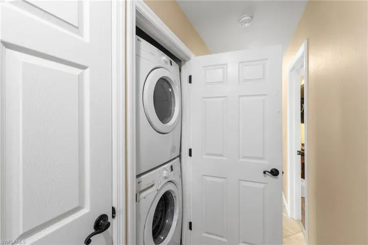 Washroom with estacked washer and dryer and light tile patterned floors