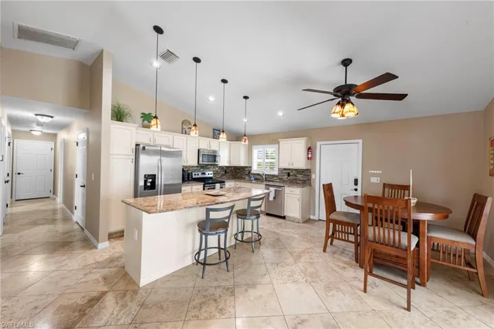 Kitchen featuring stainless steel appliances, hanging light fixtures, a kitchen bar, light stone counters, and a kitchen island