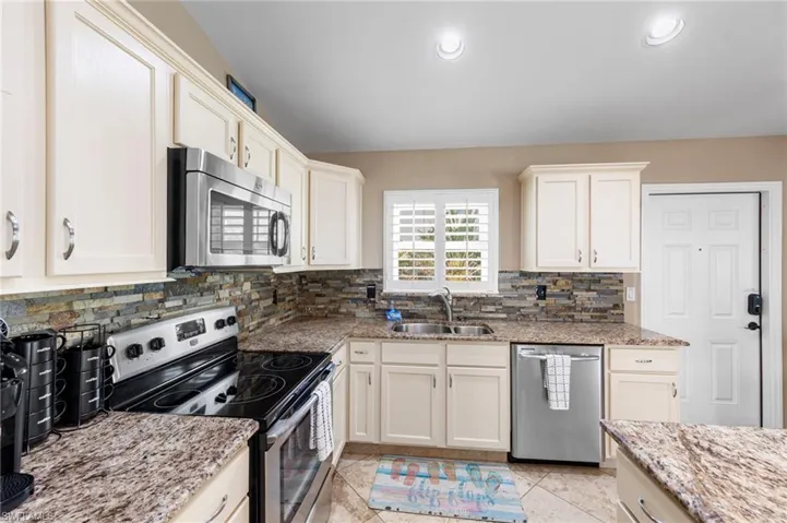 Kitchen with appliances with stainless steel finishes, light stone countertops, backsplash, recessed lighting, and white cabinets