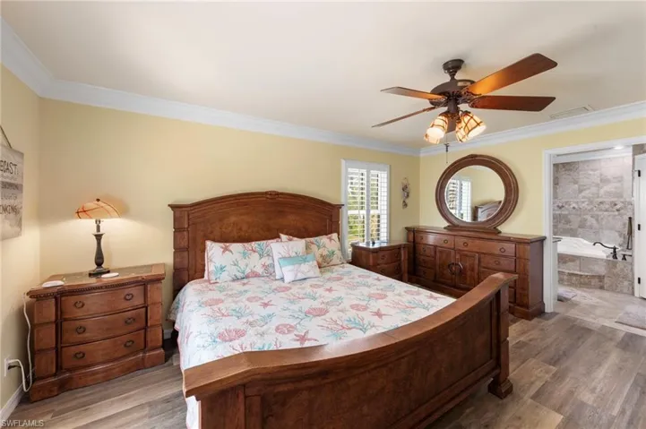 Bedroom with wood finished floors, ornamental molding, ceiling fan, and connected bathroom
