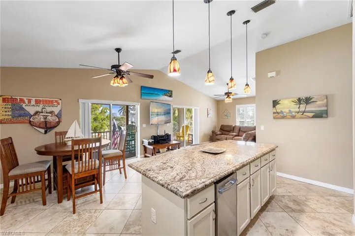 Kitchen with light stone countertops, open floor plan, a center island, pendant lighting, and vaulted ceiling