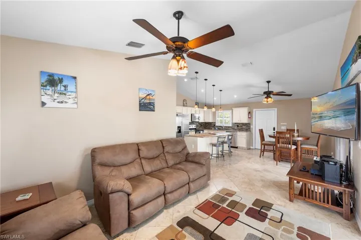 Living room featuring vaulted ceiling, a ceiling fan, and light tile patterned floors