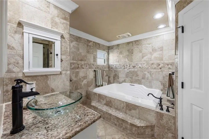 Bathroom with tile walls, a bath, ornamental molding, vanity, and recessed lighting