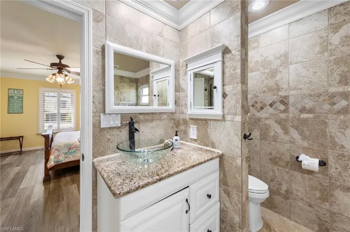 Ensuite bathroom featuring crown molding, vanity, tile walls, ceiling fan, and wood finished floors