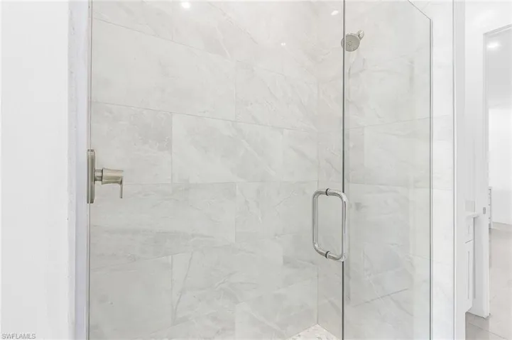 Glass-enclosed shower featuring large format tile with subtle veining, a brushed nickel shower control, and a rain shower head