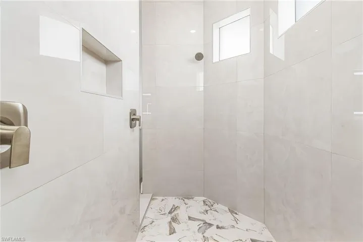 Shower stall with large format white tile walls, a built-in shower niche, and a contrasting patterned tile floor