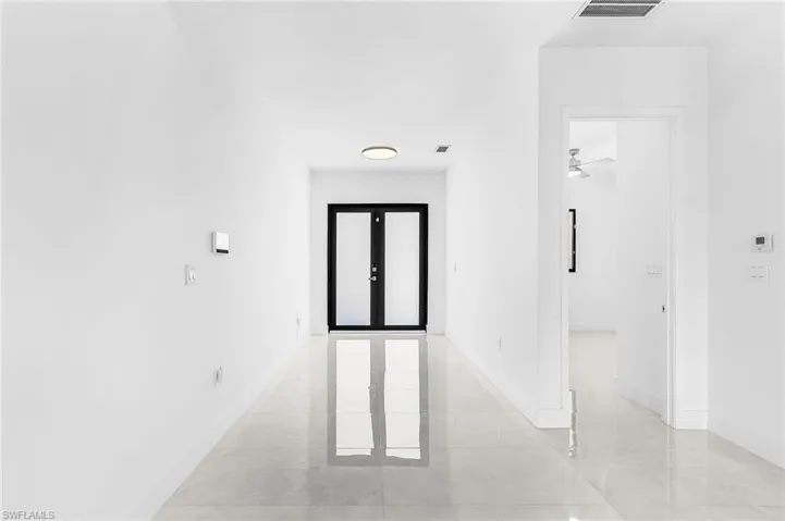 Entryway featuring a black double-door with frosted glass inserts, polished tile flooring, white baseboards, and a flush-mount ceiling light