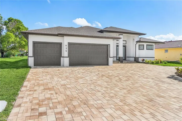 Contemporary exterior featuring a paver driveway, two-car garage, white stucco facade with dark trim, and a covered entry