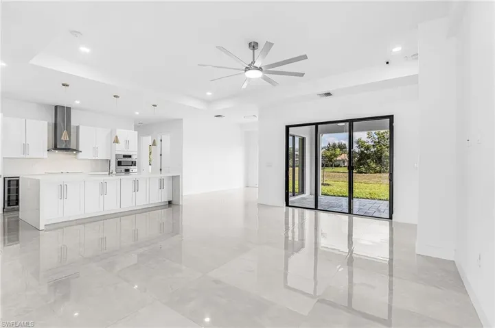 Open-concept kitchen and living area featuring polished tile flooring, a large island with integrated storage, white cabinetry, stainless steel appliances, and a beverage refrigerator