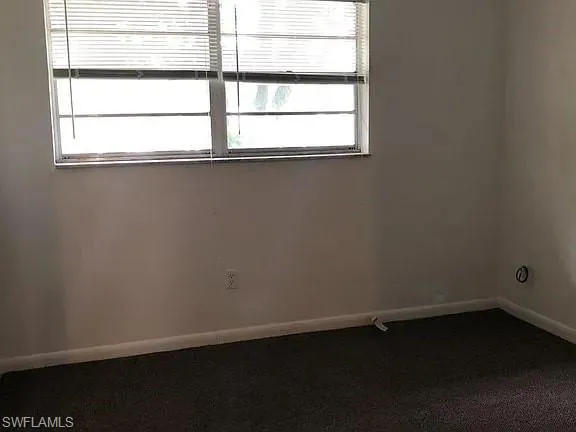 Unfurnished room with baseboards and dark carpet