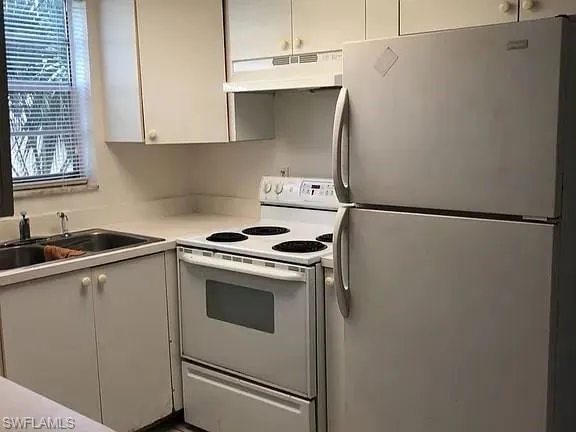 Kitchen featuring freestanding refrigerator, white range with electric cooktop, under cabinet range hood, light countertops, and white cabinets