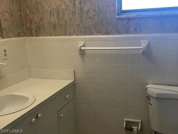 Half bath featuring vanity, wallpapered walls, and tile walls