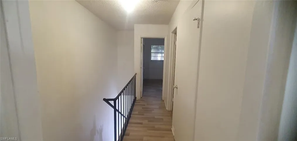 Hall featuring a textured ceiling, light wood-style flooring, and an upstairs landing