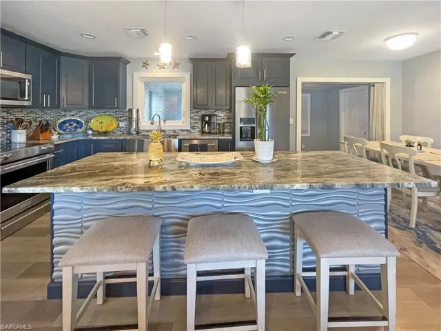 Kitchen with stainless steel appliances, light stone countertops, and light wood-style flooring